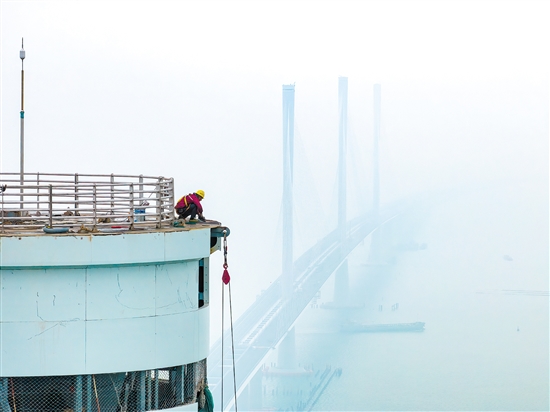 建設(shè)者在塔柱上施工，遠(yuǎn)處“海上長(zhǎng)龍”若隱若現(xiàn)。