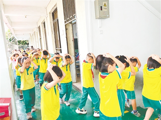 演練中，學(xué)生雙手抱頭、緊貼墻角，按照指定的逃生路線快速有序地撤離至操場(chǎng)安全區(qū)域。